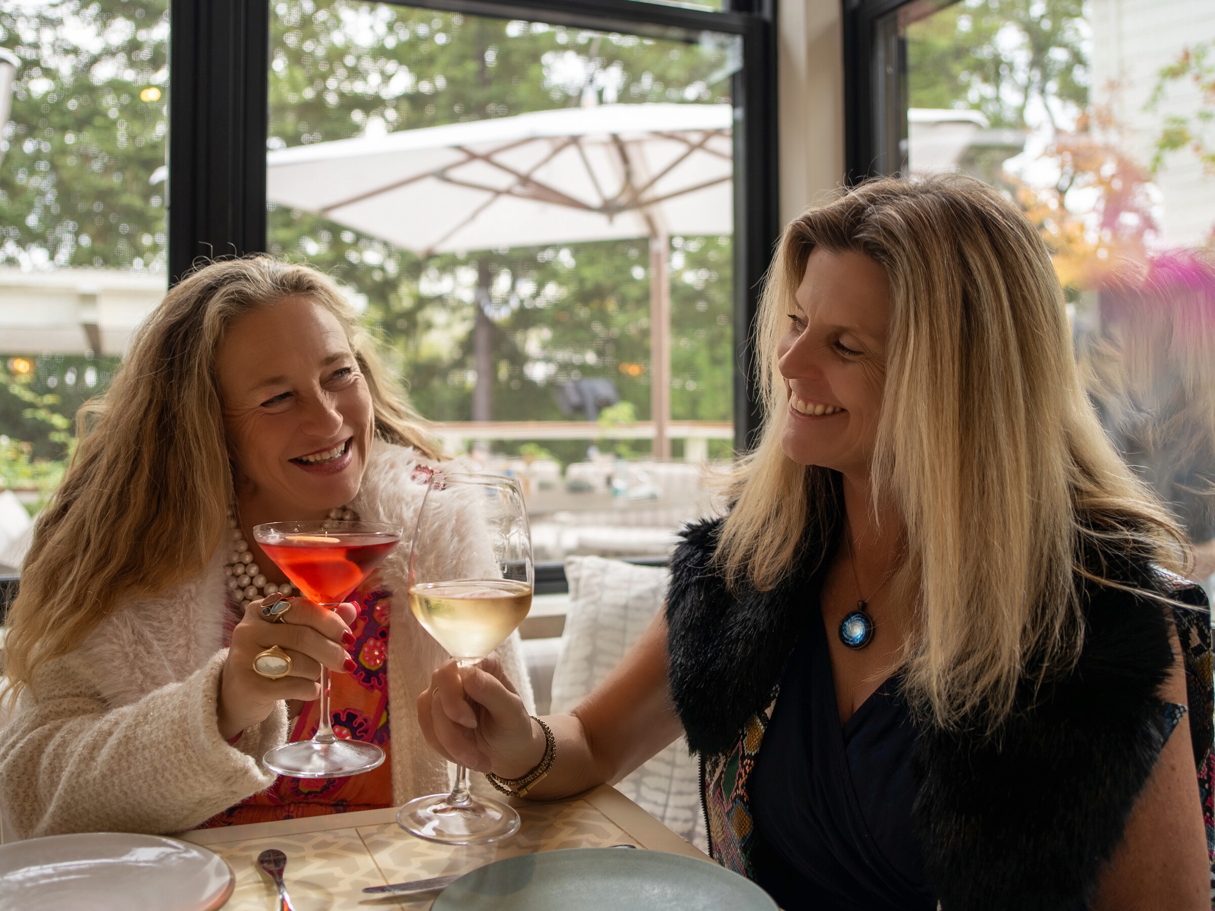 Shiloh Sophia and Amy Ahlers raising a toast at an outdoor cafe